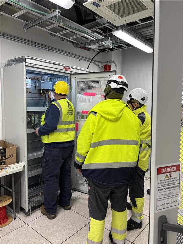 Technicians working on Hitachi auxiliary control cabinet during commissioning