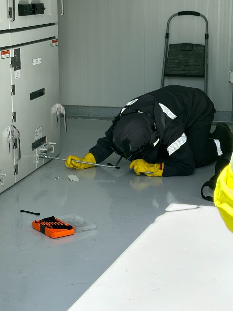 Technician in arc-rated PPE performing commissioning work on indoor electrical switchgear